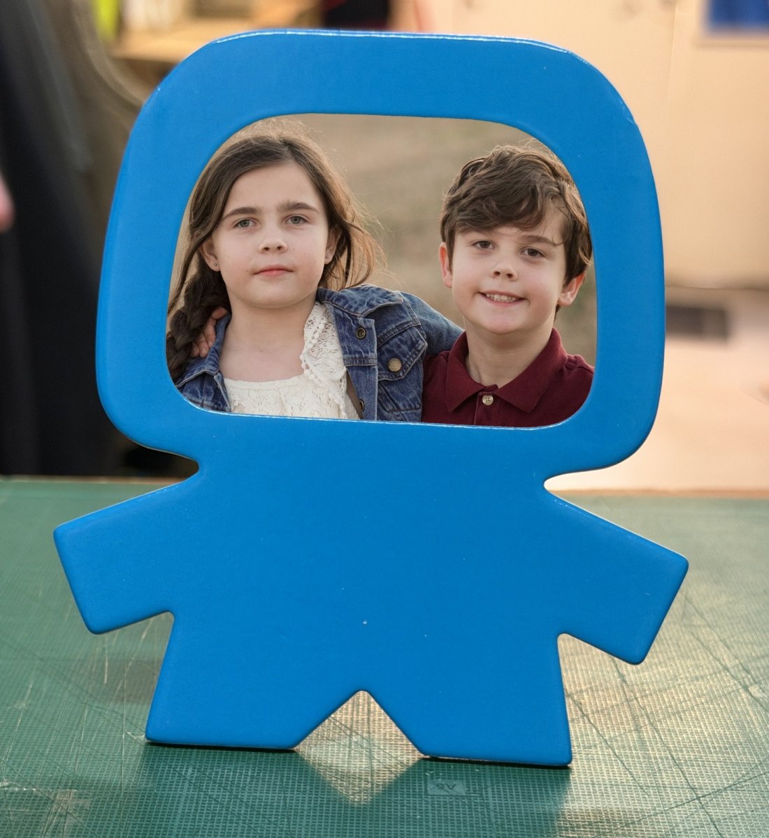 Portafotos infantil de cartón azul con forma de muñeco y la foto de dos hermanos en el hueco de la cara